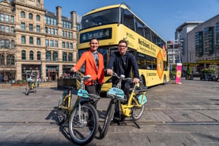 Andy Burnham and Dame Sarah Storey stand with yellow shared bikes in front of a matching bus