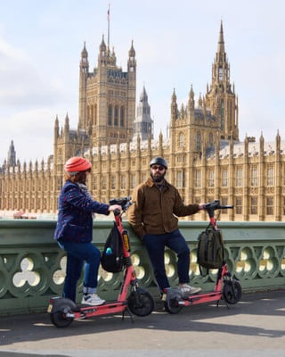 Two e-scooter riders chatting outside the Houses of Parliament