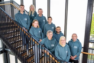 GO Travel Solutions staff pose for a team photo on a staircase in their matching blue/green hoodies
