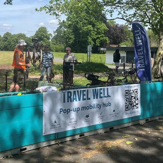 The Nottingham pop-up hub where Dr Bike mechanics are fixing bikes for residents. A Travel Well banner on the side of the turquoise structure shows information about the facilities.