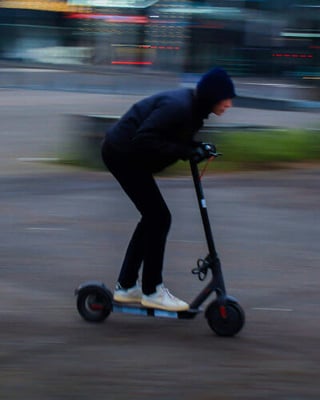 A private e-scooter rider in a lowered position wearing a hoodie, dark jeans and white trainers.